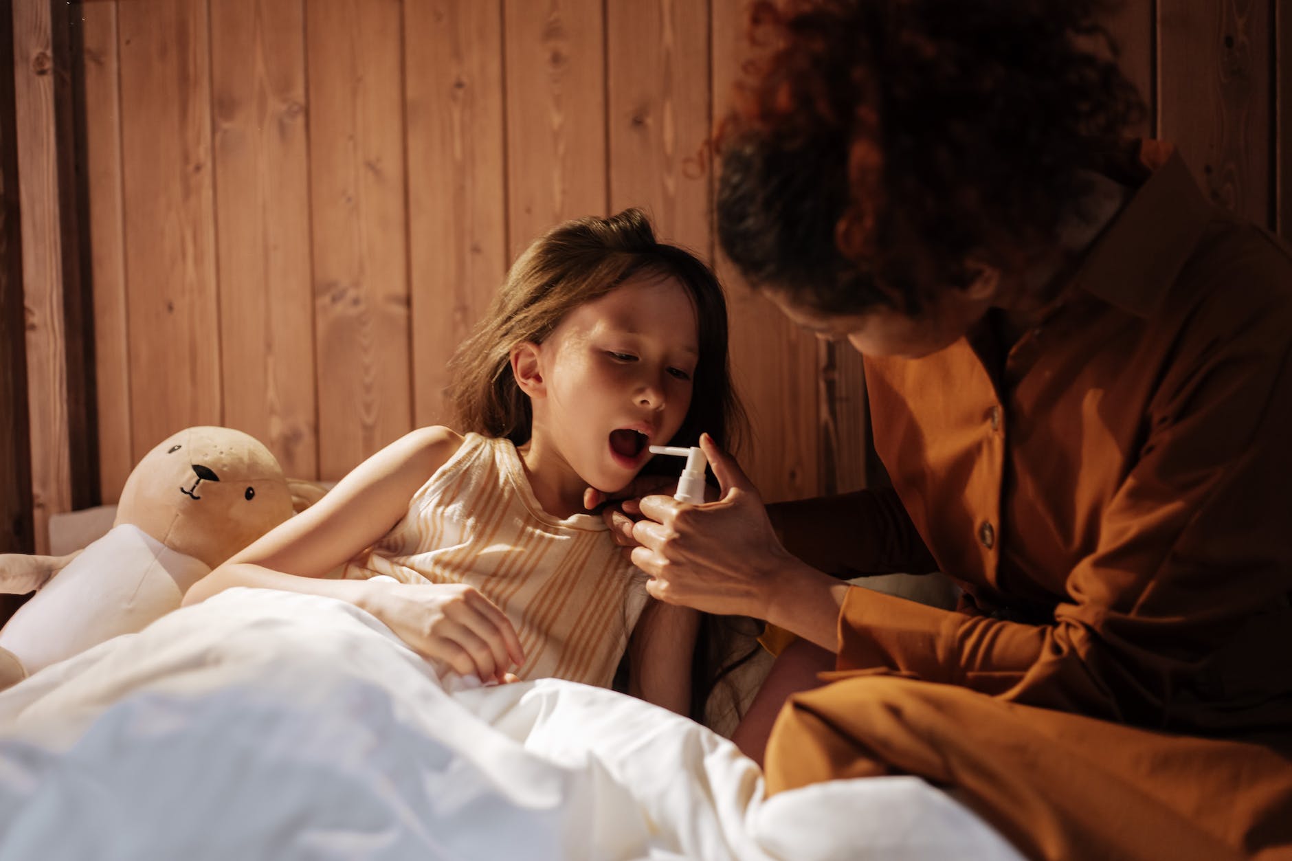 mother giving her daughter medical treatment for flu before bedtime